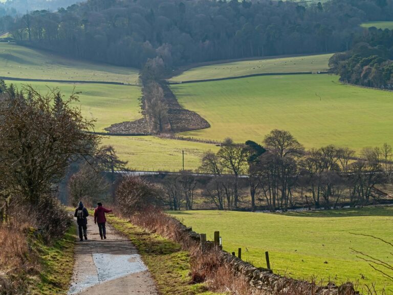 Two hikers enjoy a scenic trail through Peebles, Scotland, with rolling hills and greenery.