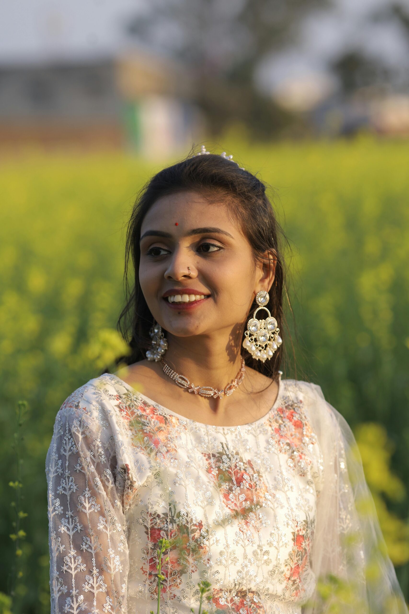 Young woman in Indian traditional attire smiling in a vibrant mustard field, showcasing cultural elegance.