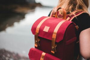 Close-up of a person with red backpack by a serene lakeside.